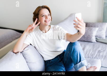 Belle brune assise sur son canapé en prenant une photo d'elle-même à la maison dans le salon Banque D'Images