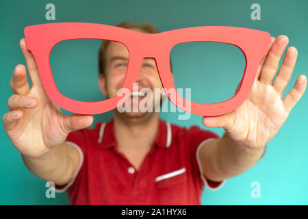 Cheerful man in a red shirt détient big red lunettes. Banque D'Images