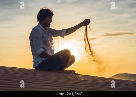 Un homme verse du sable dans le désert. Entre les doigts de sable de la notion. Banque D'Images