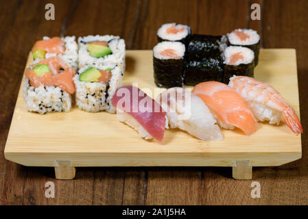 Mélange de sushi, sushi roll et nigiri avec saumon, thon, loup de mer, crevettes, avocat servi sur une plaque de bois, table en bois sombre contexte Banque D'Images