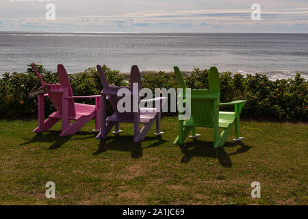 Vide, trois chaises de couleur vive sur l'herbe, avec vue sur l'océan Atlantique à White Point Beach, en Nouvelle-Écosse, Canada. Banque D'Images