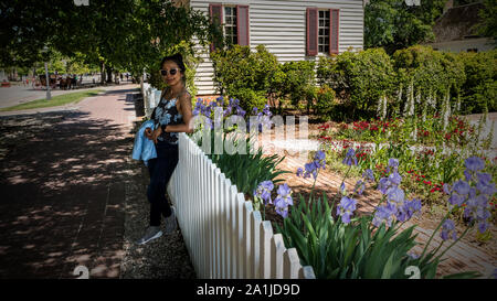 Thai woman leaning against clôture blanche en face de fleurs colorées et traditionnelles maison coloniale Banque D'Images