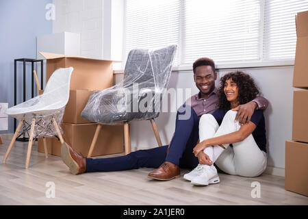 Jeune couple assis sur le plancher à l'intérieur de leur nouvelle maison Banque D'Images