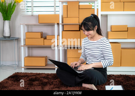 Charmante belle asiatique propriétaire adolescent femme d'affaires travailler assis sur le plancher pour le magasinage en ligne, à l'ordre dans un ordinateur portable avec l'équipement de bureau, e Banque D'Images