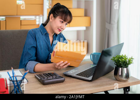 Charmante belle asiatique propriétaire adolescent femme d'affaires travailler à la maison pour faire des achats en ligne, de contrôler les détails dans la boîte aux lettres avec un ordinateur portable avec l'équipement de bureau, Banque D'Images