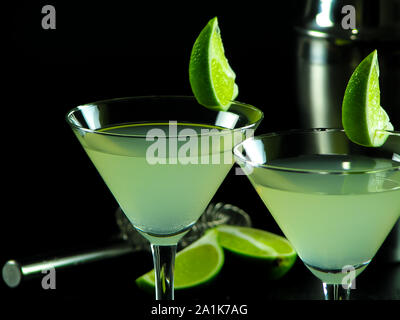 Cocktail sans alcool Daiquiri vert clair en verres à cocktail conique, décoré de tranches de citron vert, sur un fond sombre floue de shaker, tamis Banque D'Images