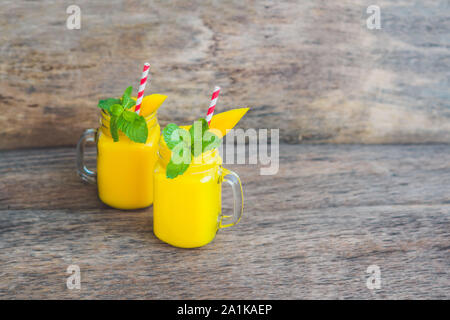 Smoothie juteux à la mangue dans deux pots en verre de maçon avec paille rouge rayée sur fond de bois ancien. Concept de vie saine, espace de copie Banque D'Images