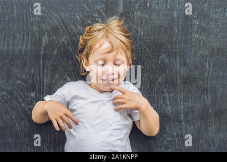 Vue de dessus d'une petite blonde enfant garçon avec de l'espace pour le texte et les symboles sur le vieux fond de bois. Concept de confusion, de réflexion et de choix Banque D'Images