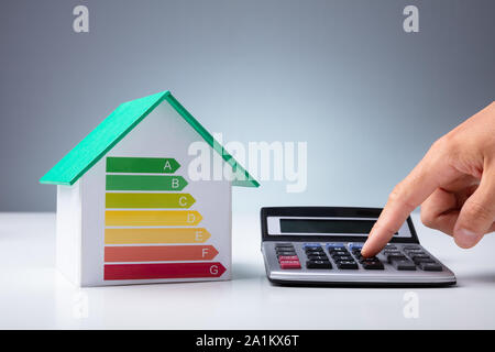 Maison miniature montrant le taux d'efficacité énergétique près de personne utilisant calculatrice sur 24 Banque D'Images