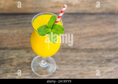 Smoothie juteux de mangue en verre avec paille rouge rayée et feuille de menthe sur fond de bois ancien. Concept de vie saine, espace de copie Banque D'Images