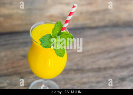 Smoothie juteux de mangue en verre avec paille rouge rayée et feuille de menthe sur fond de bois ancien. Concept de vie saine, espace de copie Banque D'Images