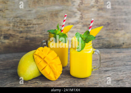 Smoothie juteux à la mangue dans deux pots en verre de maçon avec paille rouge rayée sur fond de bois ancien. Concept de vie saine, espace de copie Banque D'Images