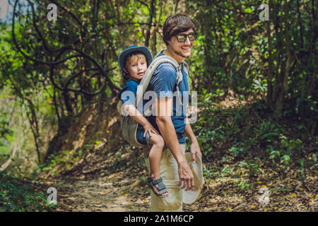 Le père porte son fils dans un bébé porte est en randonnée dans la forêt. Tourist porte un enfant sur son dos dans la nature du Vietnam Banque D'Images