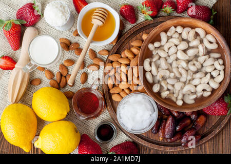 Fraise, sirop d'érable, écrous, hiney, cococnut bauuter,citron, dates. Ingrédients pour gâteau au fromage aux fraises préparation végétalien premières Banque D'Images