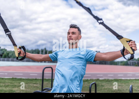 Athlète masculin, forte en été en ville, l'exercice avec des anneaux, boucles, sangles trx pour l'exercice des muscles pectoraux, d'entraînement de forme physique de la formation. Actif Banque D'Images