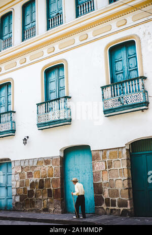 Vieil homme colombien habillé traditionnellement utilise stick de marcher dans les rues de porte turquoise typique de San Gil, Santander, Colombie Banque D'Images