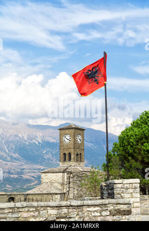 La tour de l'horloge et Abanian drapeau le Château Forteresse Gjirokaster avec montagnes et ciel bleu avec des nuages blancs en arrière-plan. Banque D'Images