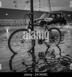 L'emblématique taxi noir de Londres par les éclaboussures de l'eau inondation suite à de fortes pluies à Londres. Banque D'Images