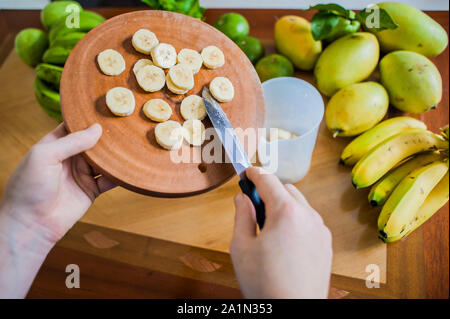 Banane en tranches sur la planche à découper les mains des femmes sont placées dans le bol du blender Banque D'Images