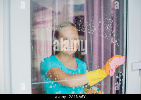 Belle femme de ménage faisant les travaux ménagers tout en utilisant un spray, laver les fenêtres Banque D'Images
