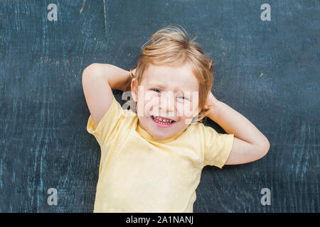 Vue de dessus d'une petite blonde enfant garçon avec de l'espace pour le texte et les symboles sur le vieux fond de bois. Concept de confusion, de réflexion et de choix Banque D'Images