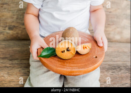 Mains tenant une planche avec des fruits frais de sapodilla sur vieux arrière-plan en bois Banque D'Images