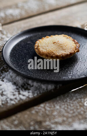 Un mince pie noire sur une plaque sur une table en bois rustique avec de la neige Banque D'Images