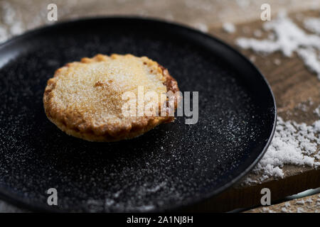 Un mince pie noire sur une plaque sur une table en bois rustique avec de la neige Banque D'Images