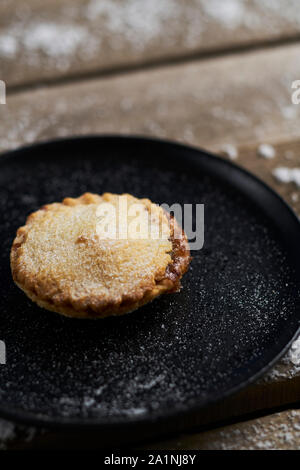 Un mince pie noire sur une plaque sur une table en bois rustique avec de la neige Banque D'Images