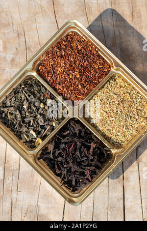 Un assortiment de quatre types de thé sec : vert, noir, feuilles de plantes supérieures, rooibos mélangé sur un fond de bois Banque D'Images