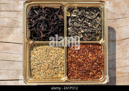 Un assortiment de quatre types de thé sec : vert, noir, feuilles de plantes supérieures, rooibos mélangé sur un fond de bois Banque D'Images