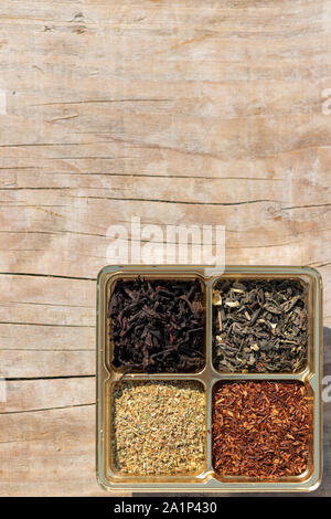 Un assortiment de quatre types de thé sec : vert, noir, feuilles de plantes supérieures, rooibos mélangé sur un fond de bois Banque D'Images