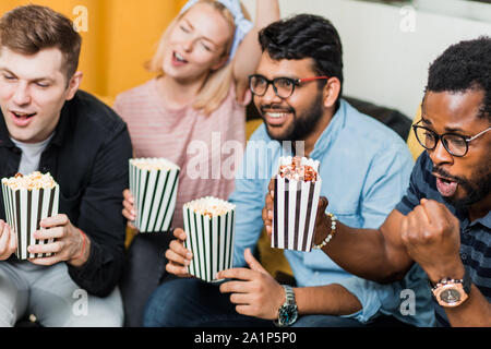 Quatre amis heureux watching sport match en direct, à la télé, eating popcorn et célébrer la victoire. Sport, loisirs, bonheur, enterta Banque D'Images