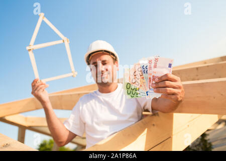 Jeune homme avec des billets et une maison symbolique dans ses mains Banque D'Images