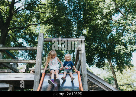 Deux jeunes enfants en haut d'une diapositive sur une structure de jeu entouré d'arbres Banque D'Images