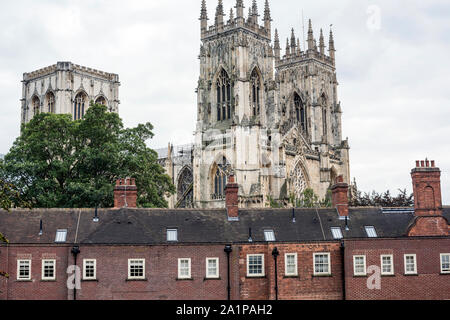 Flèches et toit de la cathédrale York Minster, UK, en arrière-plan, s'élevant au-dessus de toits de bâtiments originaux, vu contre ciel nuageux. Banque D'Images