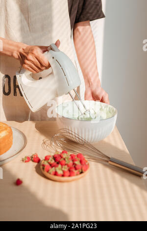 Fouetter la crème mains d'hommes blancs dans un bol en verre avec le mélangeur sur table en bois. Décisions ou gâteau Red Velvet Cake Banque D'Images