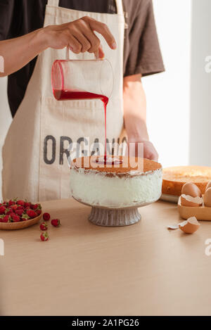 Male pastry chef pouring confiture ou sirop dans morceau de gâteau délicieux sur table en bois Banque D'Images