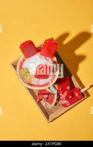 L'humeur de l'été, et des tranches de pastèque pastèque glace sur le plateau de bois sur fond jaune Banque D'Images