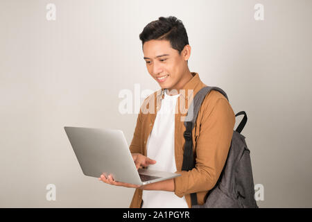 Un beau jeune étudiant en utilisant ordinateur portable et sac à dos de transport isolé sur fond blanc Banque D'Images