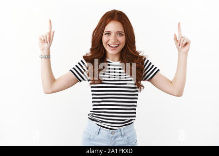 Bonne-vivante à la rousse femelle en T-shirt à rayures de rire heureusement, pointant vers le haut, les doigts soulevé haut présenter copie espace promo, appareil photo look satisf Banque D'Images