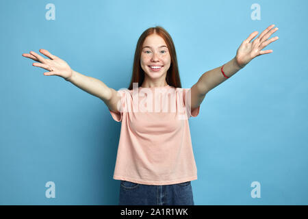 Beauitul fille positive portant des T-shirt rose sur fond bleu isolées regardant la caméra en souriant à bras ouverts pour l'accolade. L'expression joyeuse. c Banque D'Images