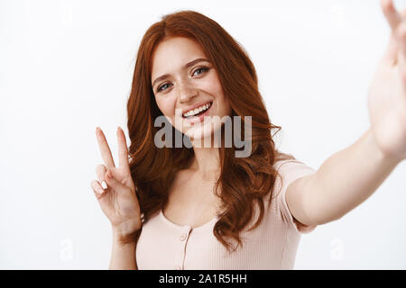 Close-up friendly optimiste redhead girl with freckles en blouse, tenez l'appareil, en tenant une main sur selfies smartphone, à la borne positive et joyeuse, show Banque D'Images