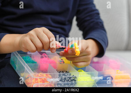 Mains garçon bracelet tisse des bagues en caoutchouc à la maison sur le canapé Banque D'Images