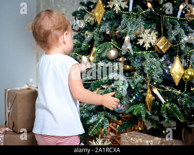 Méconnaissable petit bébé touche décoration d'arbre de Noël. Mignon bébé fille 2 ans décore l'arbre de Noël Banque D'Images