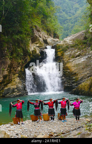 Les cheveux longs, les femmes des minorités ethniques Yao posant devant une chute d'eau dans la zone Longsheng Rizières en terrasses dans Ghuangxi Zhuang Région autonome de Chine, proche de G Banque D'Images