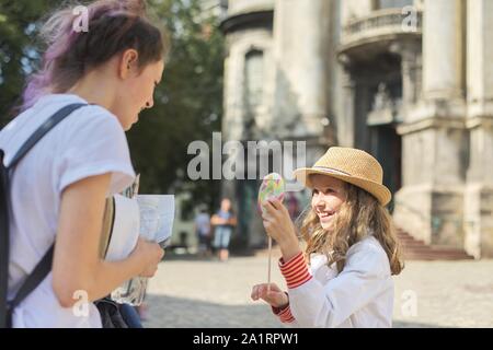 Deux enfants filles rire sœurs on city street, plus jeune avec de grands lollipop Banque D'Images