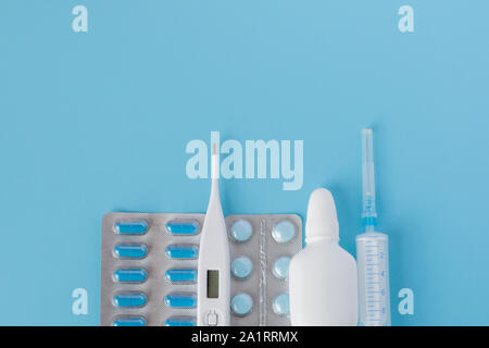 Traitement du rhume et de la grippe. Divers médicaments, un thermomètre, une pulvérisation d'une congestion nasale et une douleur dans une gorge sur un fond bleu. Copy space Banque D'Images