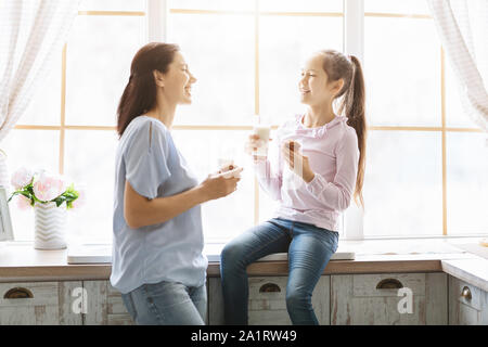 Famille heureuse de manger des muffins et boire du lait près de fenêtre de cuisine Banque D'Images