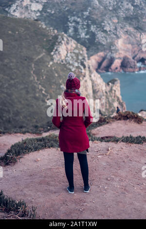 Jeune femme sur un manteau rouge en contemplant la mer depuis le haut d'une falaise Banque D'Images
